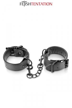 Paire de menottes en simili cuir noir avec une chaîne en métal pour une nouvelle expérience BDSM par Fetish Tentation.